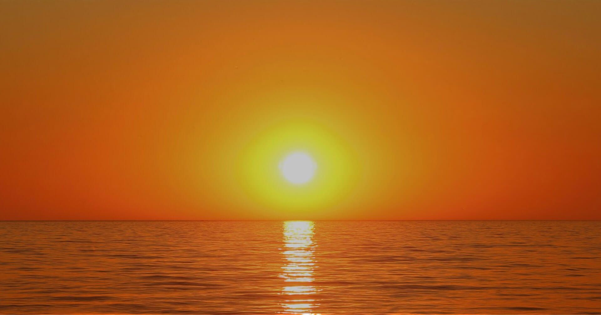 Sonnenuntergang über dem Ozean, der Himmel in warmen Farben erleuchtet, während die Wellen sanft an den Strand schlagen.